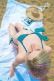 Realistic Zelex silicone love doll wearing blue bikini, standing on sandy beach